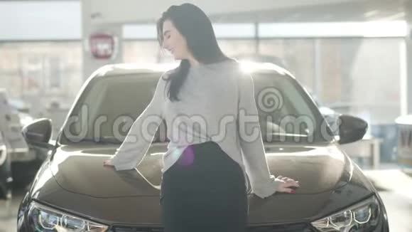 年轻自信的白种人黑发女人在新的黑色汽车旁边的阳光下摆姿势的肖像积极正面视频的预览图
