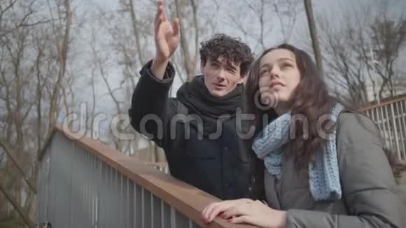 年轻的白种人男孩指着脸一个深褐色的漂亮女孩手牵着额头秋日快乐的情侣约会视频的预览图