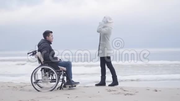 开朗的白种人女人和坐在轮椅上的男孩交谈并指着别处成年母亲和年幼残疾儿子的开支视频的预览图