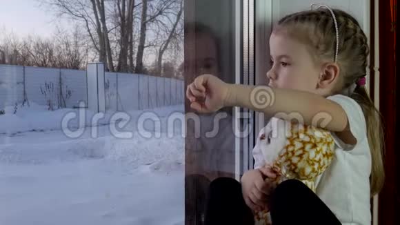 一个拿着玩具的小女孩坐在窗台上画在窗户上视频的预览图