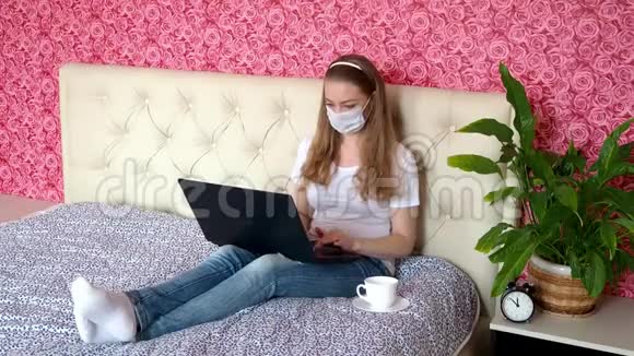 在家远程工作一个漂亮的白人女孩正在卧室里的笔记本电脑上工作床上戴着一个保护性的医疗面具c视频的预览图