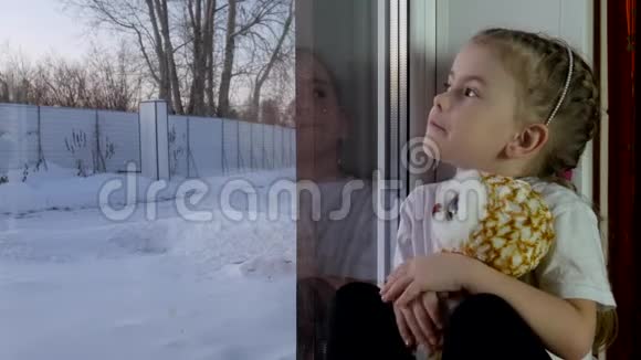 一个拿着玩具的小女孩坐在窗台上看着窗外视频的预览图