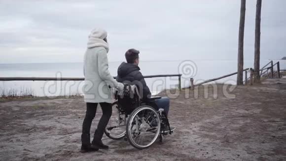 后侧的妇女滚动轮椅与年轻白种人男子沿秋河岸投标无效或母亲无效视频的预览图