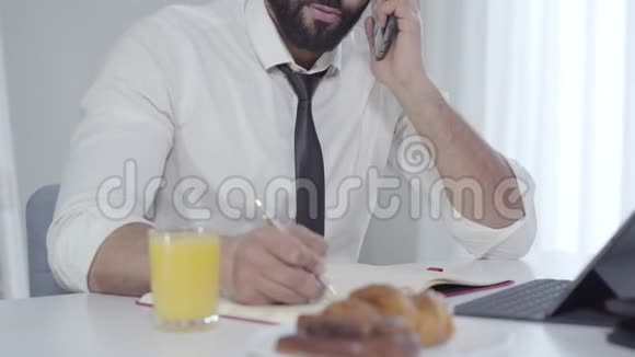 年轻英俊的中东商人打电话早上吃早餐穿白衣服的人视频的预览图