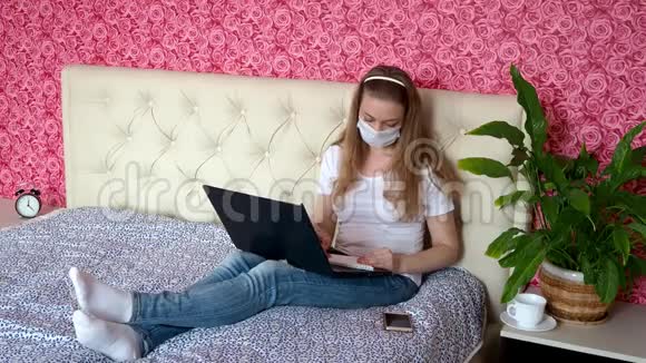 从家里远程工作一个漂亮的白种人女孩在床上的卧室里用一个保护性的医学按摩器在笔记本上写笔记视频的预览图
