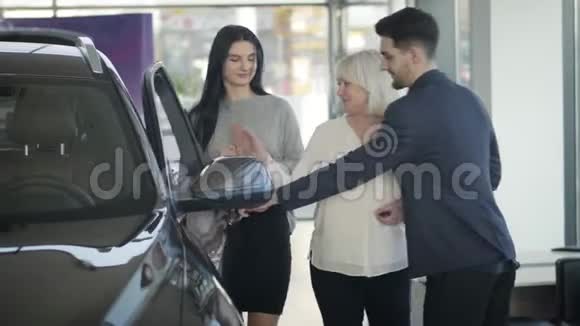 英俊的年轻白种人交易员为成熟的金发女人打开车门与美丽的黑发女人选择新汽车视频的预览图