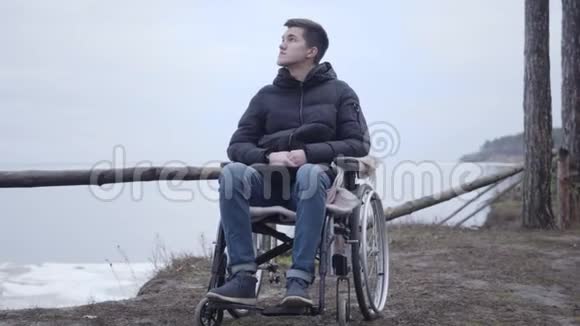 一个坐轮椅的白人残疾男孩在户外四处张望年轻的黑发男人视频的预览图