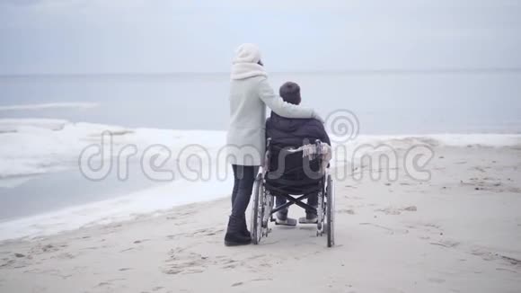 坐轮椅的成年妇女和残疾男子在沙质河岸或海边享受秋日视频的预览图