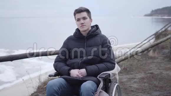 英俊的白种人残疾男孩坐在河岸上思考的肖像孤独的残废男人视频的预览图