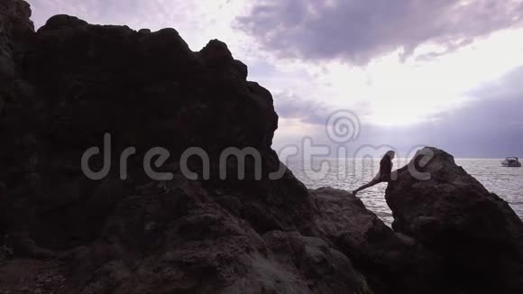 运动女孩在大海和美丽的天空的背景上做石头岩石上的分裂伸展性和灵活性视频的预览图