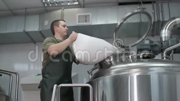 一个工作的男性啤酒厂将粉碎的麦芽倒入啤酒罐生产工艺啤酒特写视频的预览图