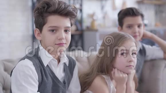 一个漂亮的白种人黑发男孩在室内摆姿势像他的孪生兄弟和可爱的小妹妹坐在视频的预览图
