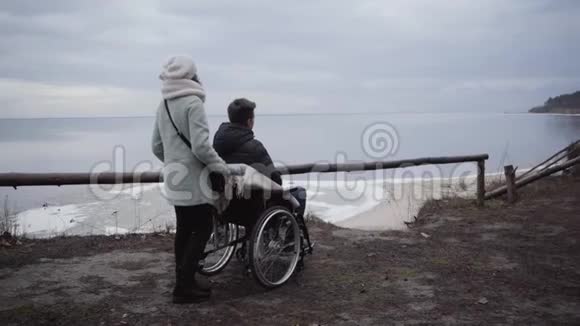 背面的妇女站在轮椅与残疾男孩在其中高加索残废人和母亲或残废人视频的预览图