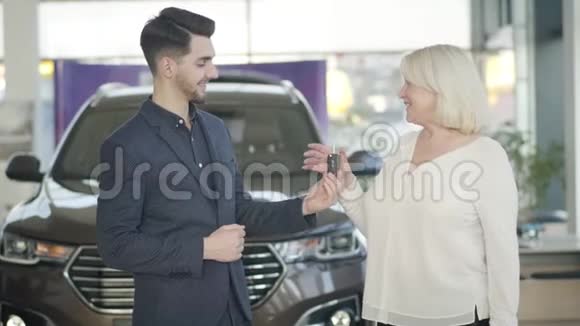 年轻积极的白种人汽车经销商在展厅给成熟开朗的女人钥匙帅气的职业男人视频的预览图