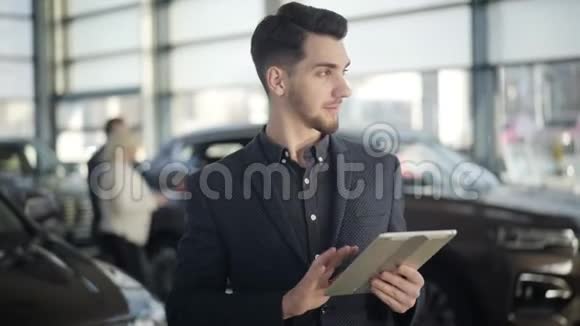年轻英俊的棕色眼睛白人男子站在汽车经销商与平板电脑看着相机和微笑自信视频的预览图