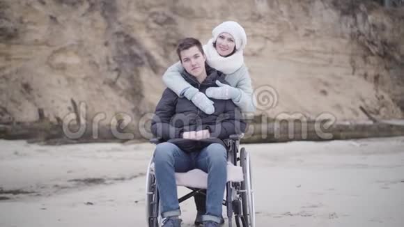 微笑的白种人女人拥抱轮椅上的残疾人的肖像年轻残疾男孩和看起来很嫩视频的预览图