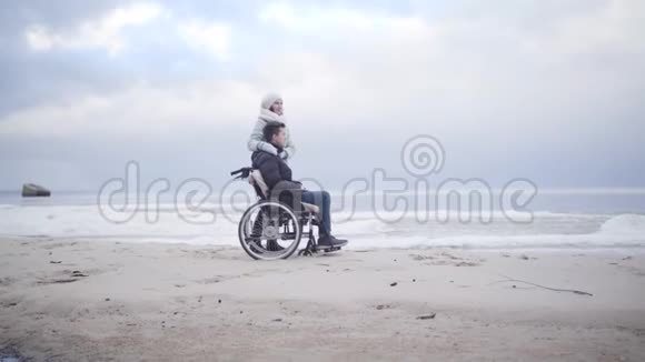 站在沙质河岸上坐轮椅的白种人年轻男女的侧面景色一幅母亲和视频的预览图