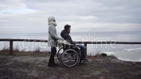 轮椅青年残疾人在河岸上用无效投标度过时间的侧视高加索成年妇女视频的预览图