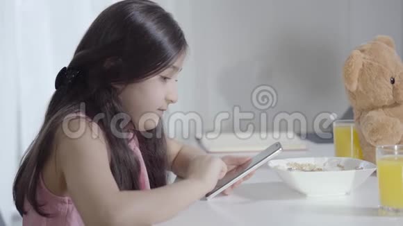早餐期间使用社交媒体集中的中东小女孩的侧视图可爱的孩子和视频的预览图