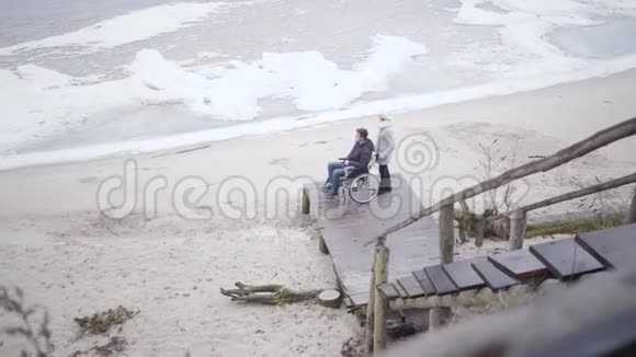 极宽的白人女人拿着轮椅和残废的男孩残疾青年及其母亲的俯视图视频的预览图