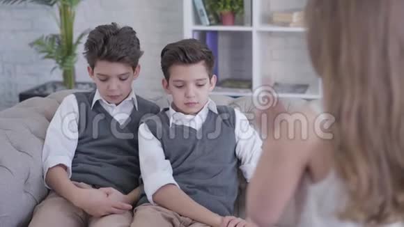 无法辨认的小白种人黑发女孩颤抖的手指骂双胞胎兄弟坐在沙发上优雅的男孩视频的预览图