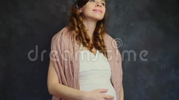 幸福的孕妇抚摸着她的腹部美丽的准妈妈在黑暗的背景上微笑视频的预览图
