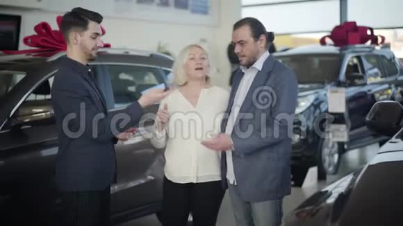 年轻的职业汽车经销商把新车的钥匙送给老两口感激的金发女人亲吻丈夫视频的预览图