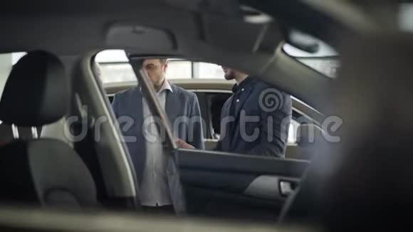 年轻的白种人汽车经销商为成熟的金发客户开门高级妇女坐在司机的座位上成功视频的预览图