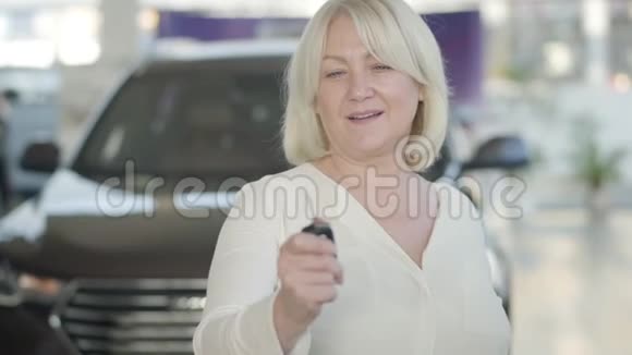 特写成熟的白种人幸福的女人在展厅炫耀汽车钥匙兴奋的金发女郎在镜头前展示钥匙视频的预览图