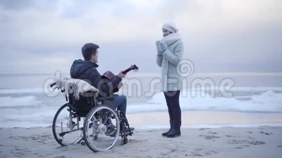 微笑着年轻的母亲拍手拥抱轮椅上的残疾儿子布鲁内特先生为父母弹吉他视频的预览图