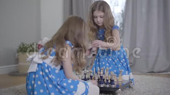 两个漂亮的白种人姐妹穿着类似的蓝色连衣裙在家下棋小双胞胎呆在家里视频的预览图