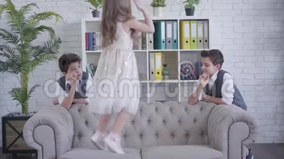 活泼开朗的白种人女孩在沙发上跳着伸着男孩手快乐的姐姐无聊的双胞胎视频的预览图