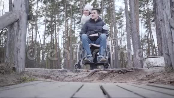 带着微笑的白种人残疾男子坐轮椅在森林里和女人在户外交谈的肖像青年残疾人视频的预览图