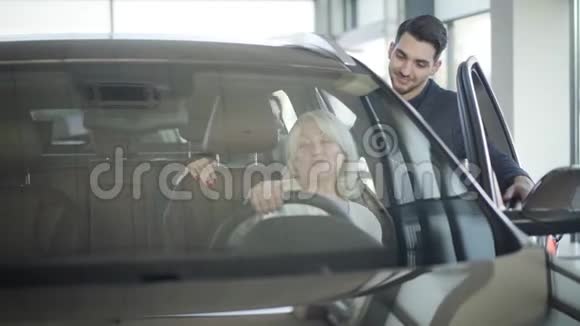 年轻的微笑汽车经销商咨询客户坐在汽车里成熟的金发女人和年轻的黑发女人视频的预览图
