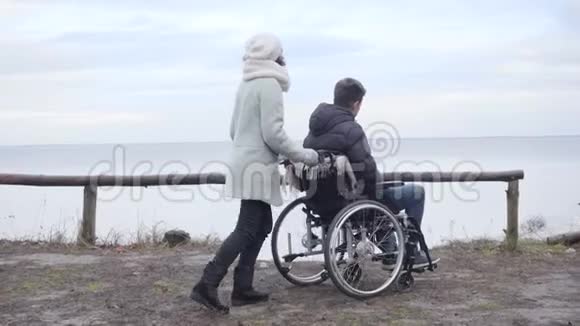 年轻的积极白人妇女停止轮椅与残疾男孩在河岸和指向母亲开支视频的预览图