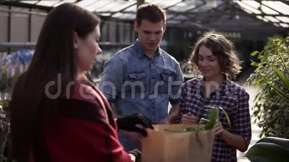 欧洲年轻夫妇正从温室里的女卖家那里从棕色纸袋中收获有机食品一个付钱的人视频的预览图