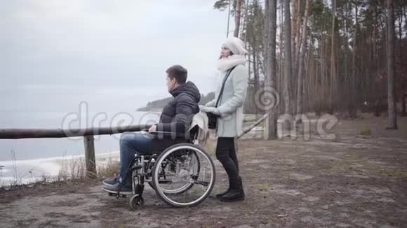 年轻的高加索女人拿着轮椅和残疾男孩说话从左到右依次移动视频的预览图