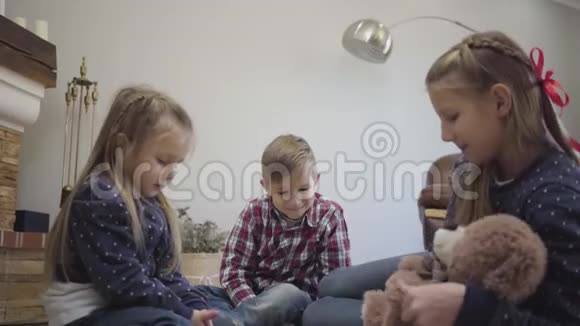 侧面看年轻的高加索女孩在家招待弟弟妹妹小女孩拿着玩具熊视频的预览图