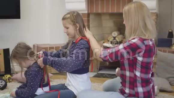 侧面看金发白种人女人梳大女儿头发她为妹妹梳辫子母亲视频的预览图