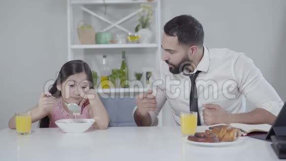 中东商人正在和吃早餐的小女孩说话指着手表父亲问视频的预览图