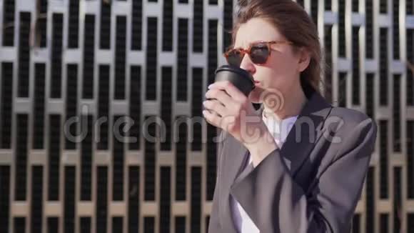 年轻的女商人正在公园里吃早餐戴墨镜的女孩喝回收纸杯中的豆咖啡视频的预览图