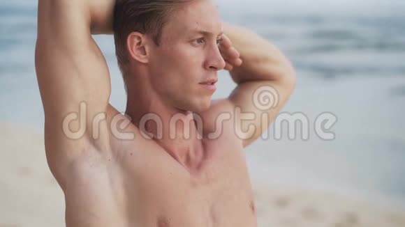 肌肉发达的金发男子在沙滩上做伸展运动的肖像视频的预览图