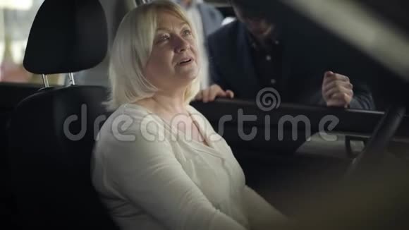 漂亮成熟的白种人女人坐在司机座位上和汽车经销商交谈的肖像自信的老太太视频的预览图