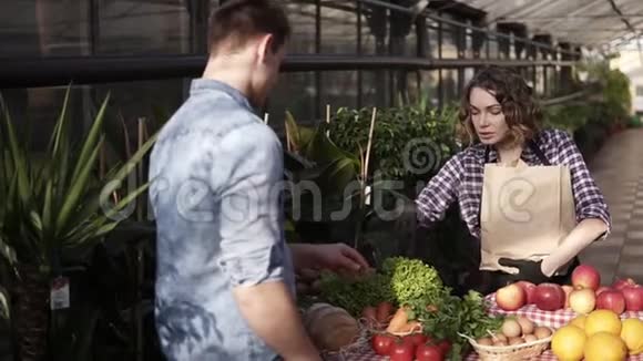 布鲁内特欧洲女售货员穿着围裙帮助顾客选择把一堆绿色沙拉放在棕色中视频的预览图