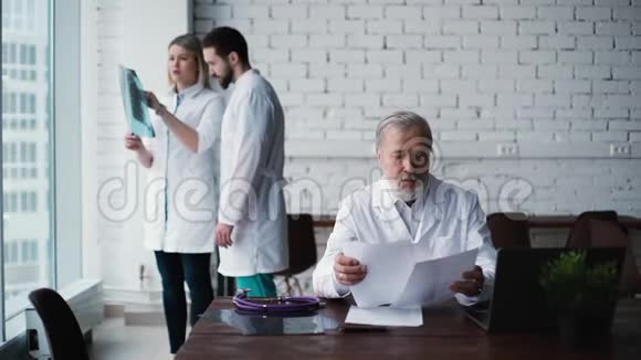 有经验的成人医生坐在他的办公桌前研究他的病人文件视频的预览图
