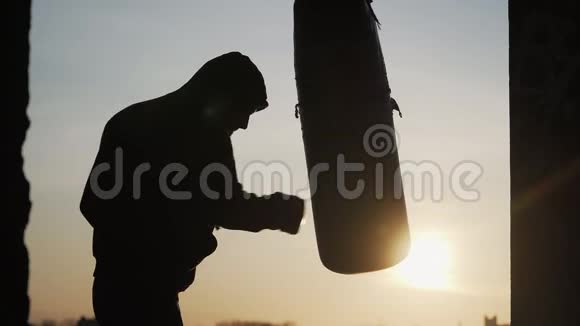 剪影男童拳手在美丽的夕阳背景下跳动着一个拳击袋体育和武术户外拳击训练视频的预览图