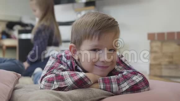 小白种人黑发男孩的肖像眼球震颤看着摄像机微笑着他的姐妹们在玩视频的预览图
