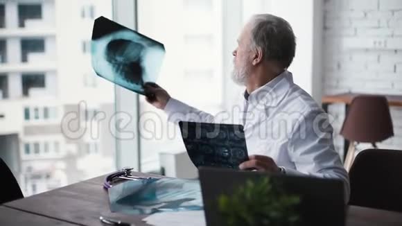 有经验的留白胡须的成年医生坐在办公桌前检查X光视频的预览图