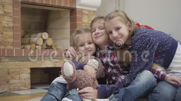 三个白人儿童看着摄像机微笑的肖像快乐的女孩和男孩在家门口拥抱视频的预览图