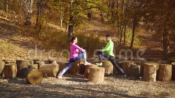 在秋天的森林里一对运动员用木头伸展腿视频的预览图